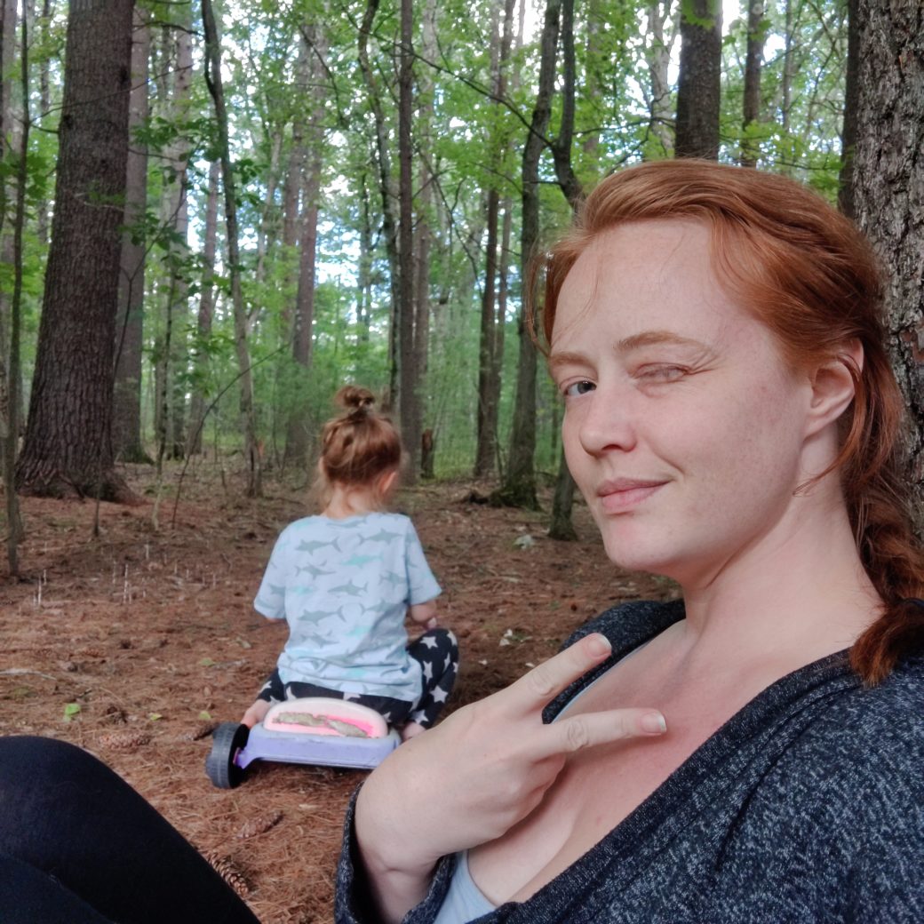 Aging isn't as bad as I thought. A picture of me sitting in the woods making a peace sign and winking. My daughter is on her bigwheel in the background.
