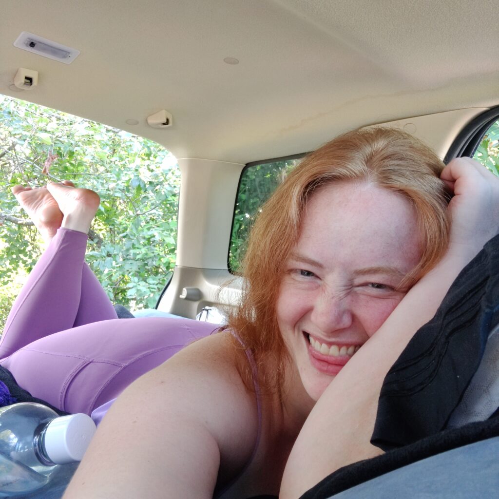 Me with a big smile, lying on an air mattress in the back of my SUV while car camping