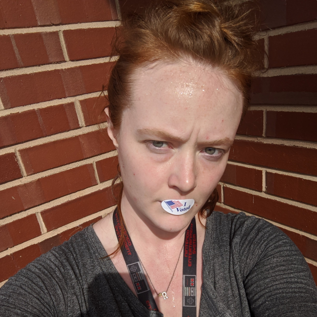 Remembering to vote is always an important little thing that you can do to make a difference. Image of me with my hair up and standing with my back in the corner of two brick walls and an "I Voted" sticker with a US flag on it stuck over my mouth.